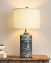 Gray ceramic table lamp with white linen shade and LED bulb on wooden surface
