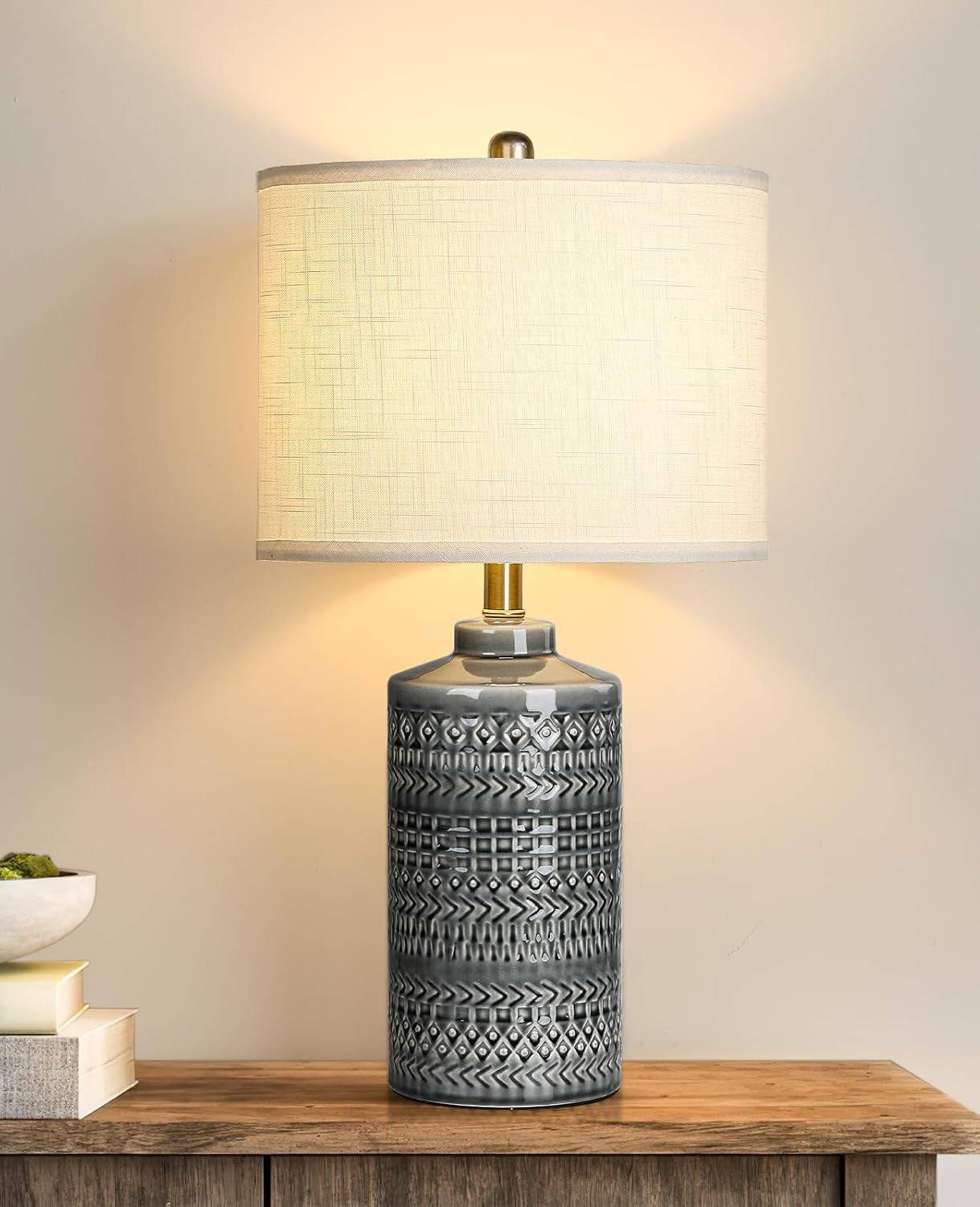 Gray ceramic table lamp with white linen shade and LED bulb on wooden surface