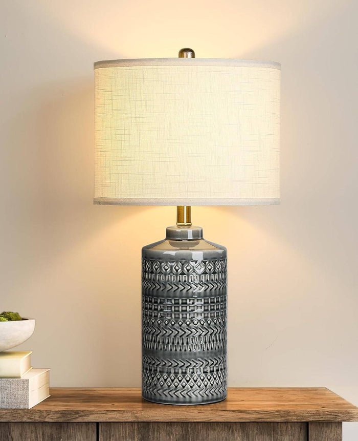 Gray ceramic table lamp with white linen shade and LED bulb on wooden surface